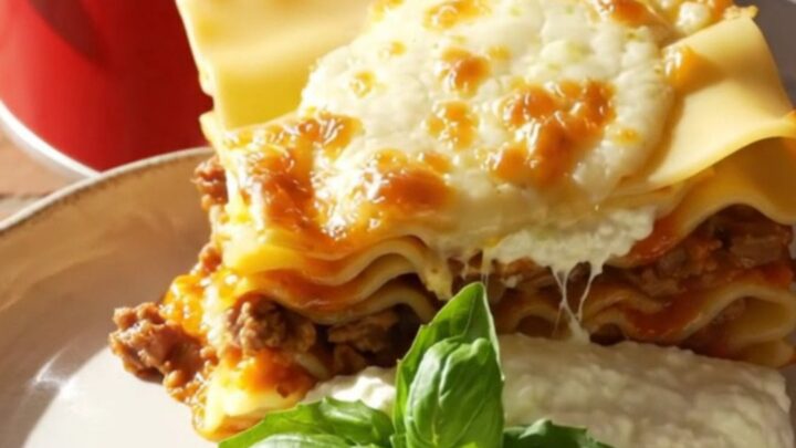A close-up of a towering square of no-boil lasagna on a plate with melted cheese and fresh basil.
