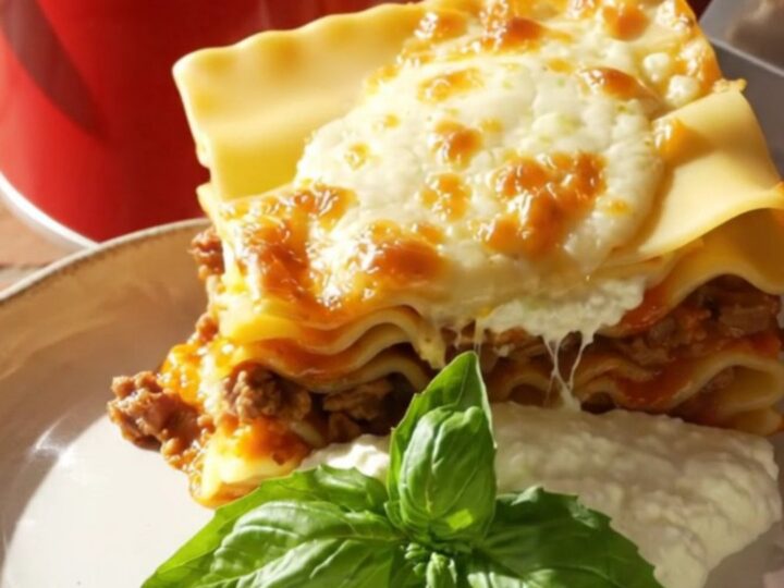 A close-up of a towering square of no-boil lasagna on a plate with melted cheese and fresh basil.