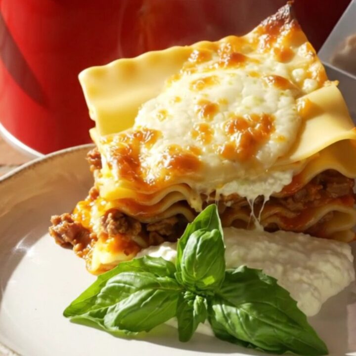 A close-up of a towering square of no-boil lasagna on a plate with melted cheese and fresh basil.