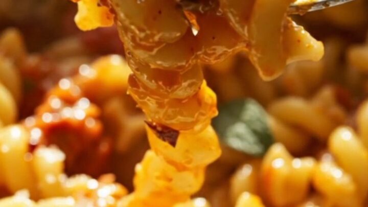 A close-up of creamy baked feta pasta with burst cherry tomatoes in a slow cooker.