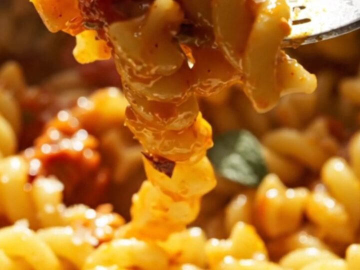 A close-up of creamy baked feta pasta with burst cherry tomatoes in a slow cooker.