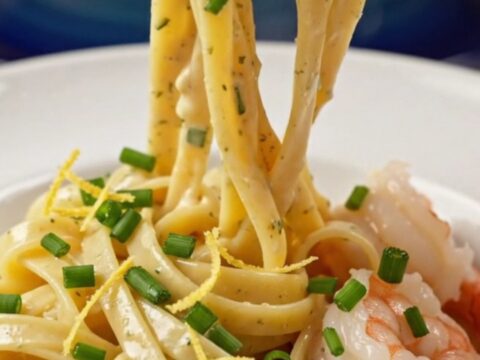 A close-up view of creamy shrimp linguine in a pasta bowl, garnished with chives and lemon zest.