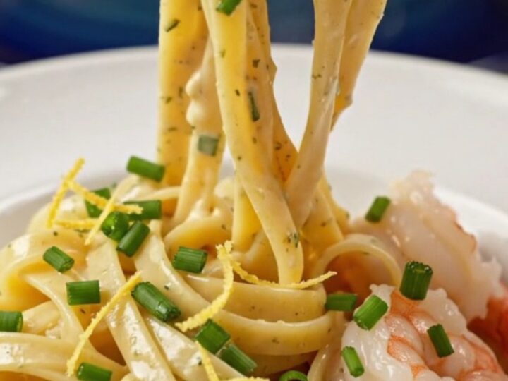 A close-up view of creamy shrimp linguine in a pasta bowl, garnished with chives and lemon zest.