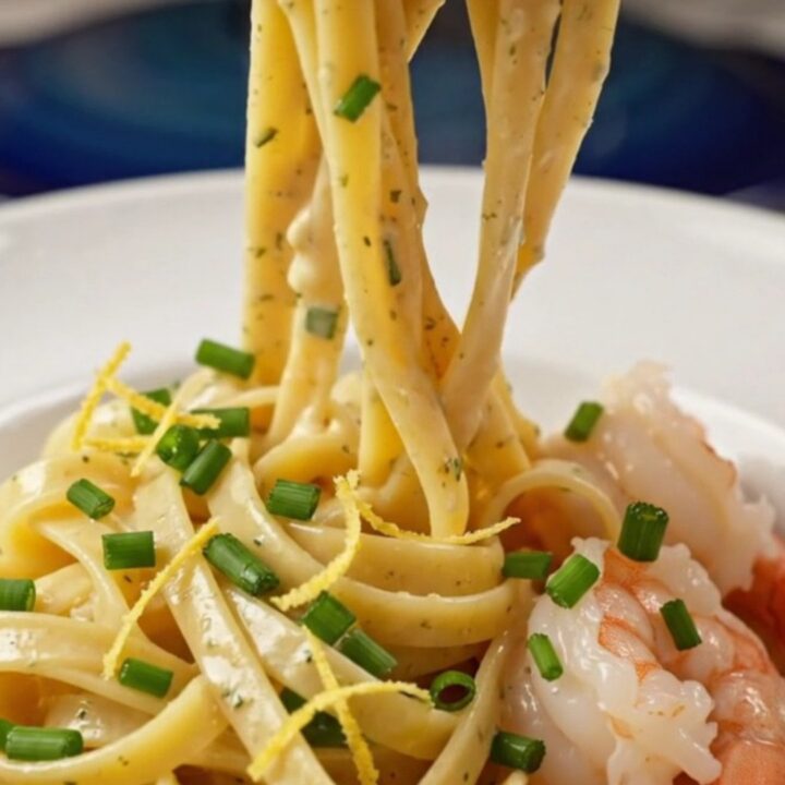 A close-up view of creamy shrimp linguine in a pasta bowl, garnished with chives and lemon zest.