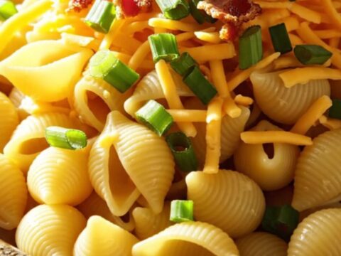 A close-up of creamy crockpot chicken bacon ranch pasta shells in a rustic stoneware bowl, topped with green onions.