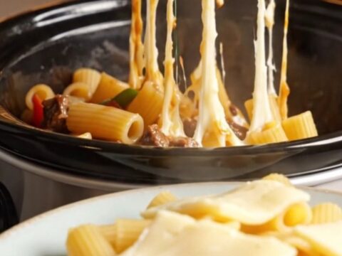 A towering plate of Philly cheesesteak rigatoni with long, gooey strings of melted provolone cheese stretching