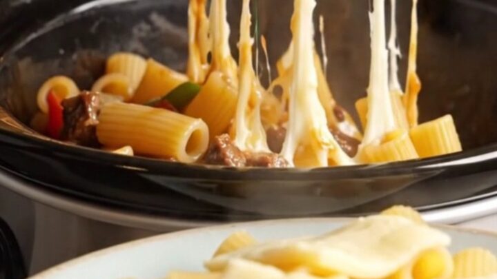 A towering plate of Philly cheesesteak rigatoni with long, gooey strings of melted provolone cheese stretching