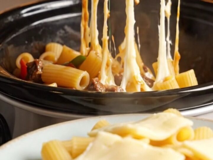 A towering plate of Philly cheesesteak rigatoni with long, gooey strings of melted provolone cheese stretching