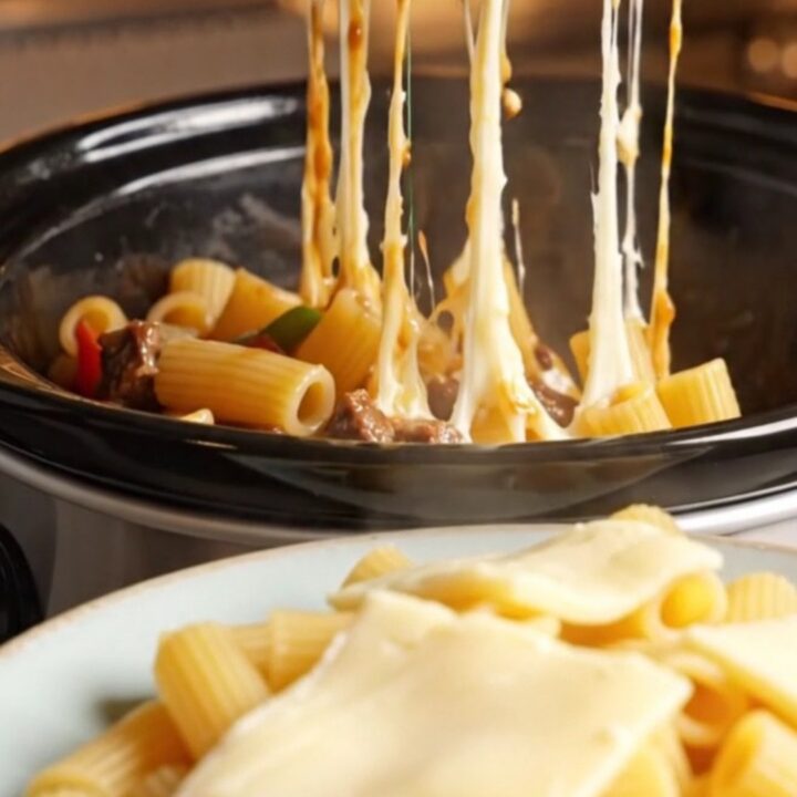 A towering plate of Philly cheesesteak rigatoni with long, gooey strings of melted provolone cheese stretching