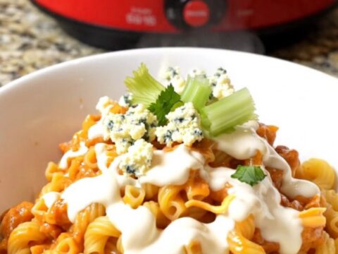 A large ceramic pot filled with creamy buffalo chicken mac and cheese topped with crumbled gorgonzola and fresh celery.