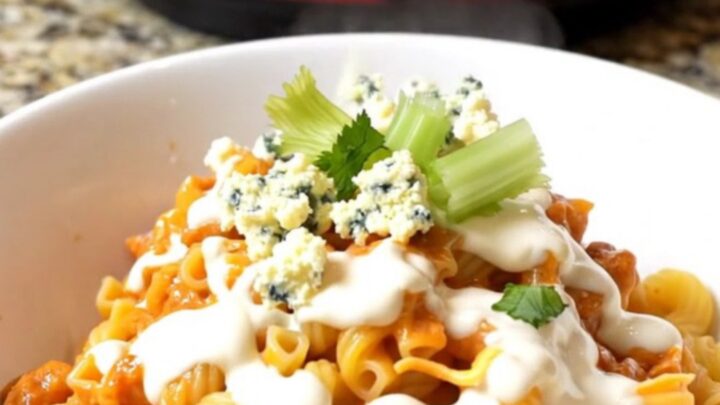 A large ceramic pot filled with creamy buffalo chicken mac and cheese topped with crumbled gorgonzola and fresh celery.
