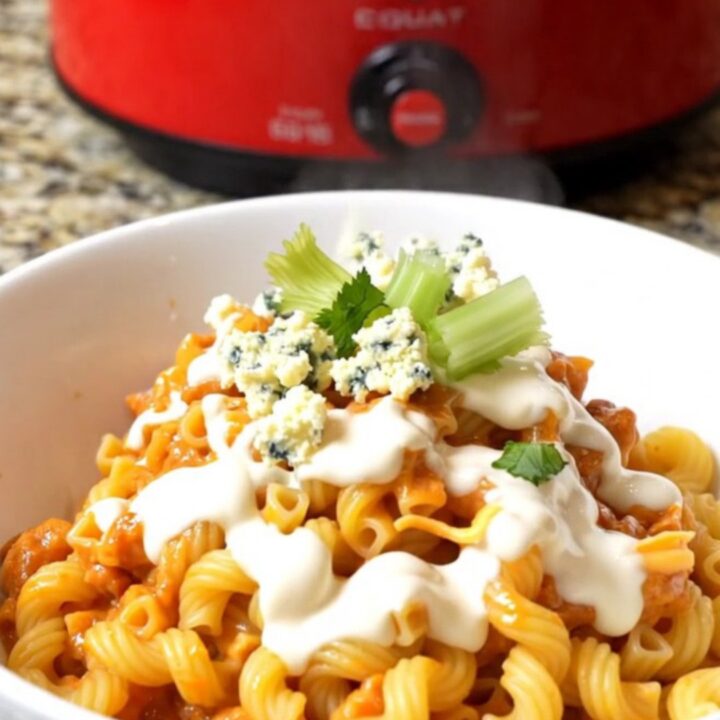 A large ceramic pot filled with creamy buffalo chicken mac and cheese topped with crumbled gorgonzola and fresh celery.