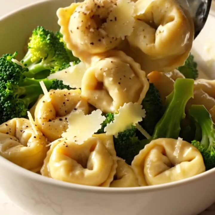 A steaming bowl of creamy chicken and broccoli tortellini topped with parmesan curls.