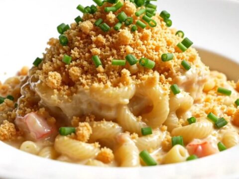 A decadent serving of lobster and crab mac and cheese in a bowl, topped with buttery cracker crumbs and fresh chives.