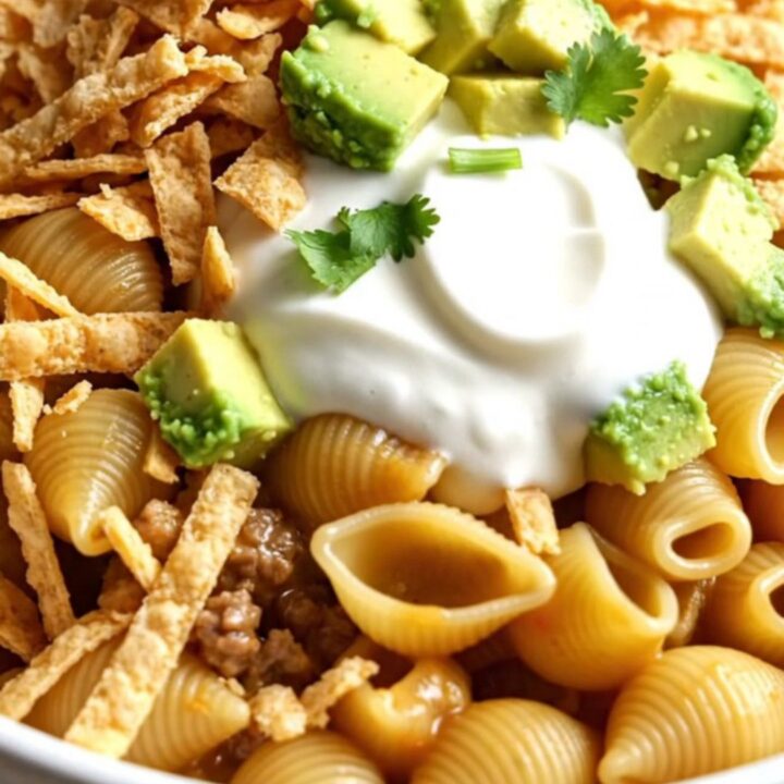A close-up of cheesy taco pasta shells in a ceramic crockpot topped with avocado, cilantro, and tortilla strips.