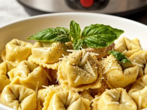 A close-up of creamy chicken tortellini in a slow cooker, garnished with basil.