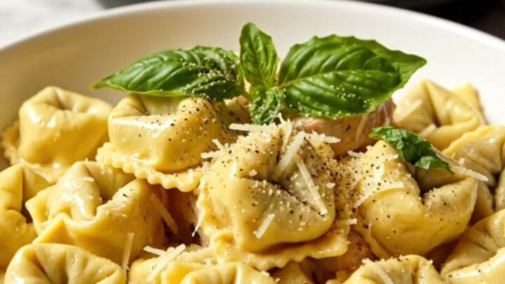A close-up of creamy chicken tortellini in a slow cooker, garnished with basil.