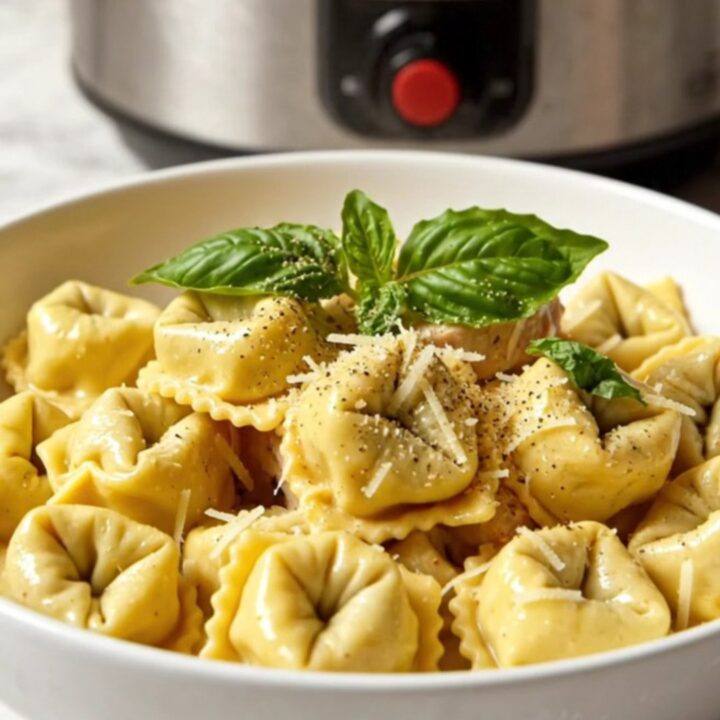 A close-up of creamy chicken tortellini in a slow cooker, garnished with basil.