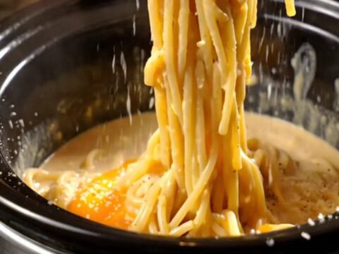 A glossy, creamy spaghetti carbonara in a black Crockpot with crispy pancetta pieces and fresh black pepper.