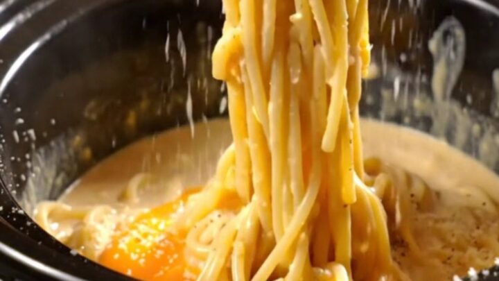 A glossy, creamy spaghetti carbonara in a black Crockpot with crispy pancetta pieces and fresh black pepper.