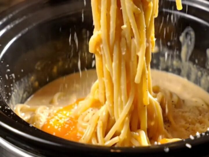 A glossy, creamy spaghetti carbonara in a black Crockpot with crispy pancetta pieces and fresh black pepper.