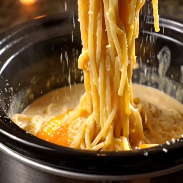 A glossy, creamy spaghetti carbonara in a black Crockpot with crispy pancetta pieces and fresh black pepper.