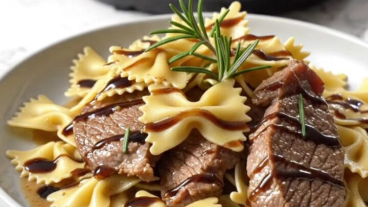 A close-up of creamy gorgonzola steak and farfalle pasta in a ceramic crockpot ready for serving.