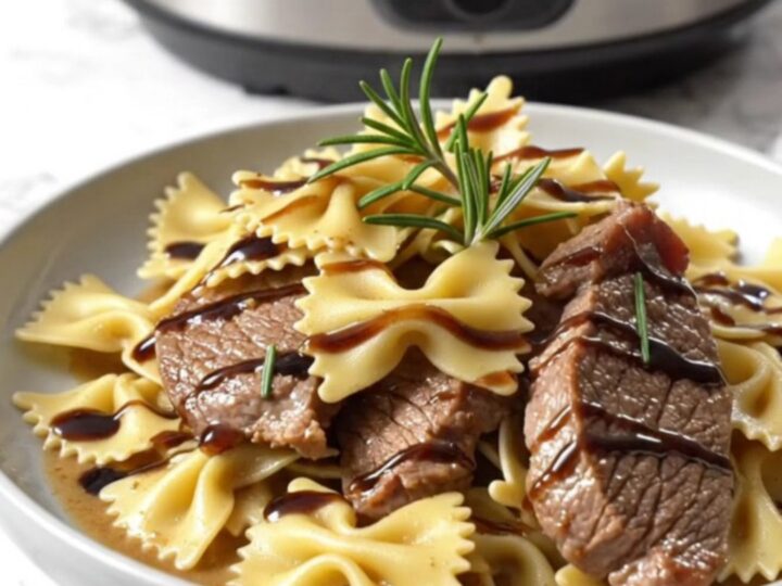 A close-up of creamy gorgonzola steak and farfalle pasta in a ceramic crockpot ready for serving.