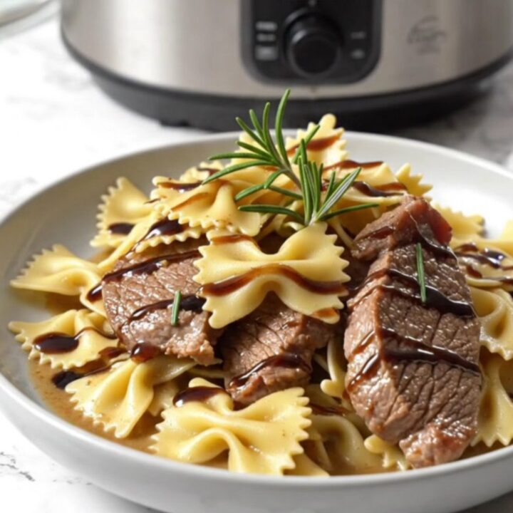 A close-up of creamy gorgonzola steak and farfalle pasta in a ceramic crockpot ready for serving.