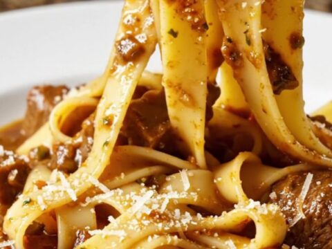 A close-up of fall-apart beef short rib ragu served over wide ribbons of fresh pappardelle in a rustic bowl.