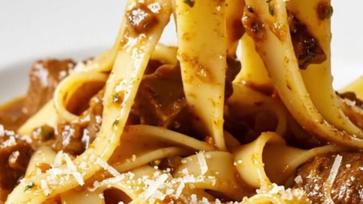 A close-up of fall-apart beef short rib ragu served over wide ribbons of fresh pappardelle in a rustic bowl.