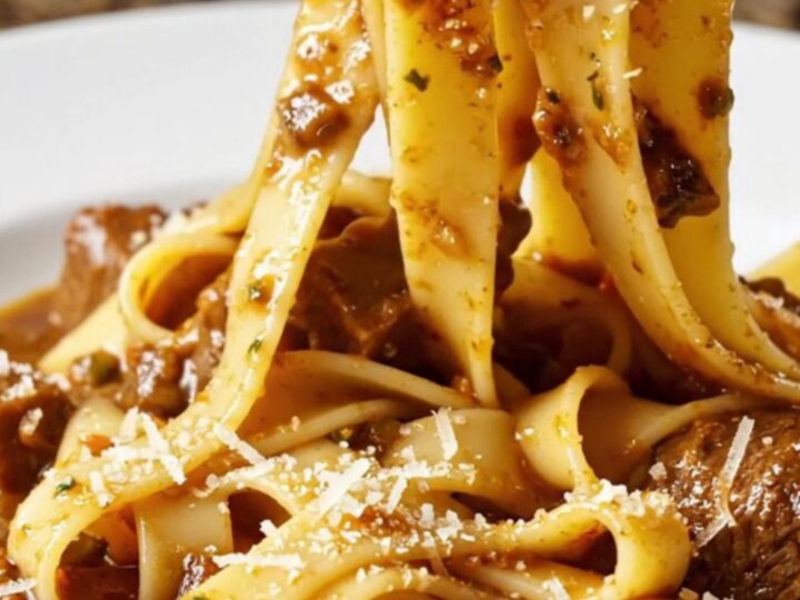 A close-up of fall-apart beef short rib ragu served over wide ribbons of fresh pappardelle in a rustic bowl.