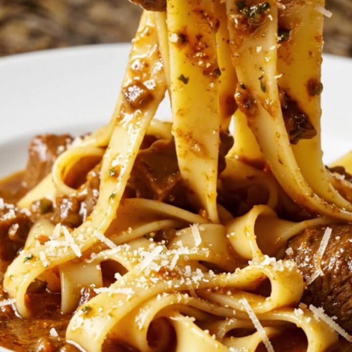 A close-up of fall-apart beef short rib ragu served over wide ribbons of fresh pappardelle in a rustic bowl.