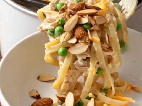 A close-up shot of creamy chicken tetrazzini with linguine, mushrooms, and melted cheese in a ceramic slow cooker.