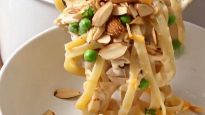 A close-up shot of creamy chicken tetrazzini with linguine, mushrooms, and melted cheese in a ceramic slow cooker.