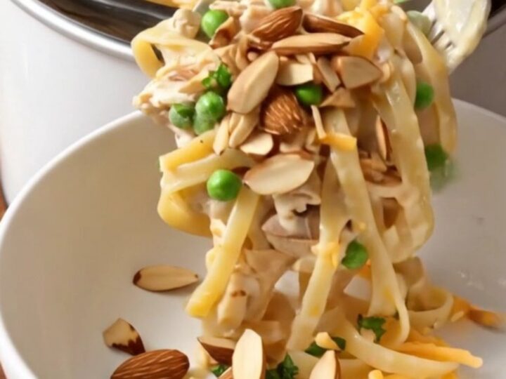 A close-up shot of creamy chicken tetrazzini with linguine, mushrooms, and melted cheese in a ceramic slow cooker.