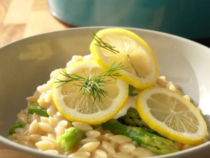 A wide ceramic bowl filled with creamy lemon orzo, tender chicken, and bright green asparagus spears.