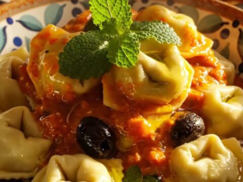 A close-up view of creamy Mediterranean tortellini with chicken and feta in a blue crockpot.