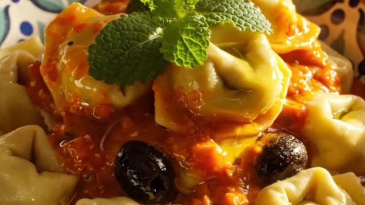 A close-up view of creamy Mediterranean tortellini with chicken and feta in a blue crockpot.