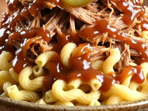 A towering bowl of creamy BBQ pulled pork mac and cheese topped with crispy fried onions and pickled jalapeños.