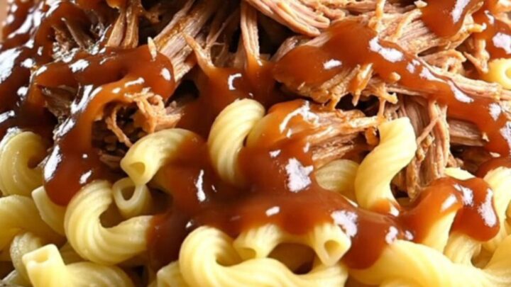 A towering bowl of creamy BBQ pulled pork mac and cheese topped with crispy fried onions and pickled jalapeños.