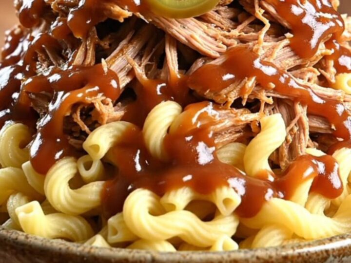 A towering bowl of creamy BBQ pulled pork mac and cheese topped with crispy fried onions and pickled jalapeños.