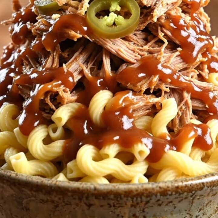 A towering bowl of creamy BBQ pulled pork mac and cheese topped with crispy fried onions and pickled jalapeños.