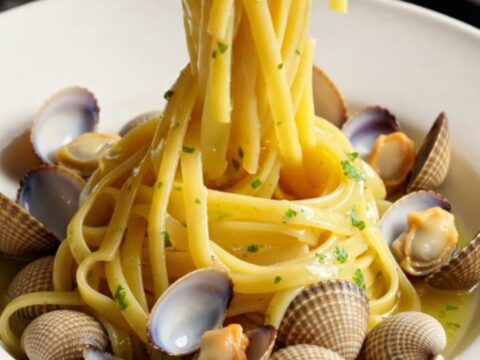 A close-up of glossy linguine with fresh clams in a rich garlic white wine sauce in a white crockpot.