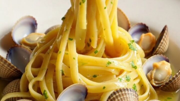 A close-up of glossy linguine with fresh clams in a rich garlic white wine sauce in a white crockpot.
