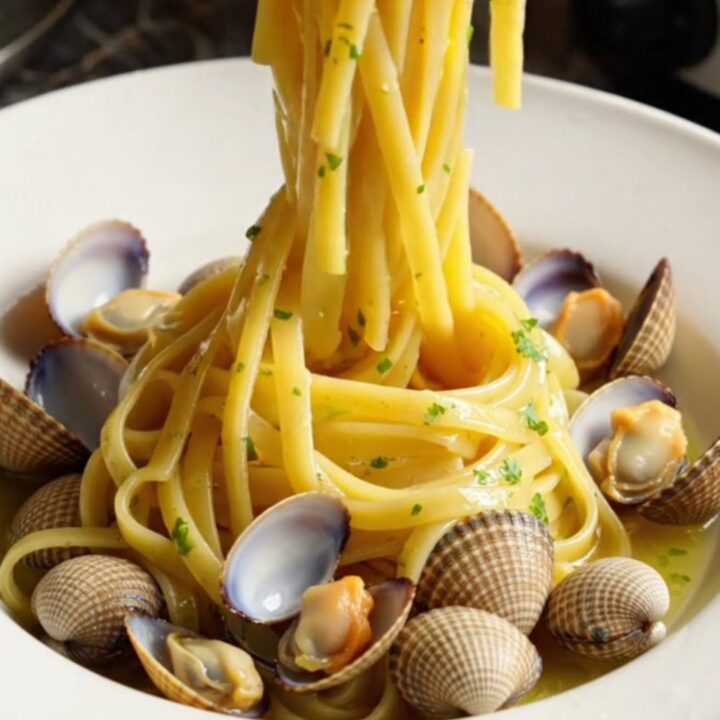 A close-up of glossy linguine with fresh clams in a rich garlic white wine sauce in a white crockpot.