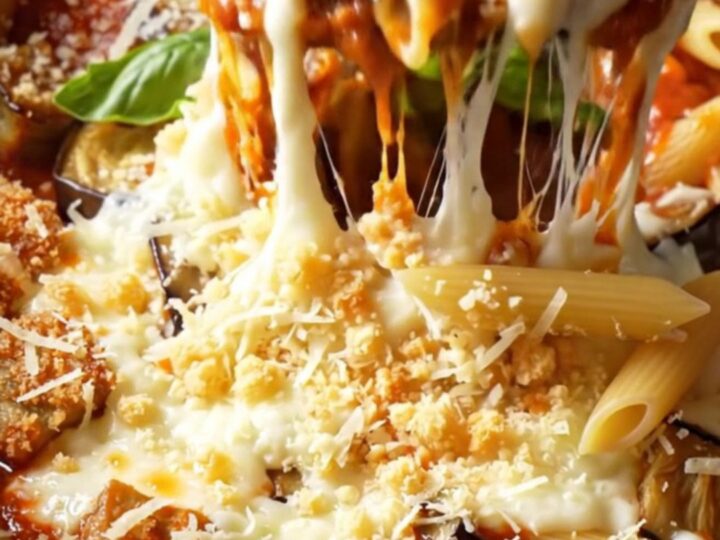 A close-up of a slow cooker filled with eggplant parmesan penne topped with melted mozzarella and fresh basil.