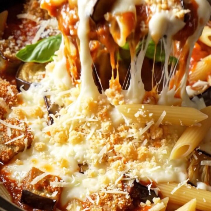 A close-up of a slow cooker filled with eggplant parmesan penne topped with melted mozzarella and fresh basil.