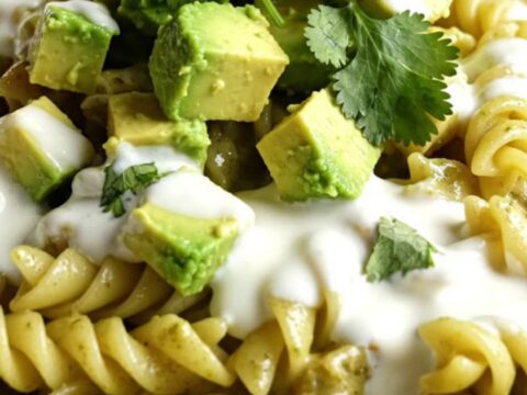 A vibrant bowl of creamy green chili chicken pasta topped with fresh avocado, crema, and cilantro.