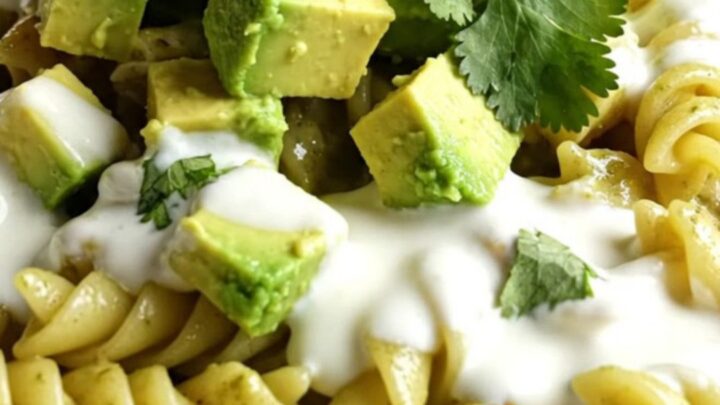 A vibrant bowl of creamy green chili chicken pasta topped with fresh avocado, crema, and cilantro.